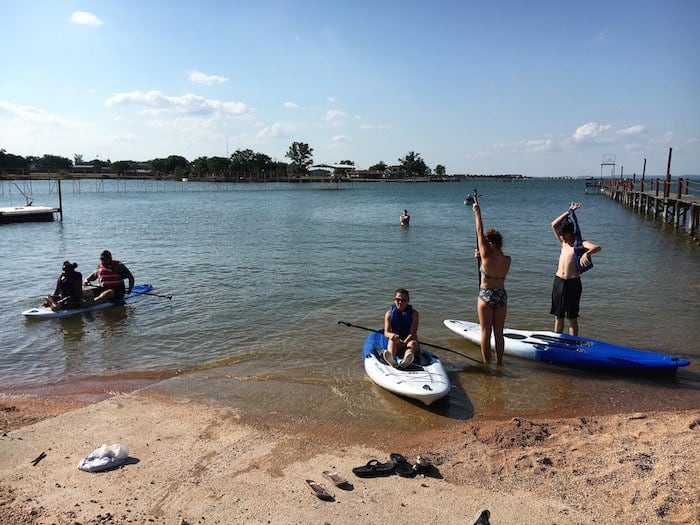Image of guests using paddle board rentals at our lake beach front. Following our Texas cabin rentals policies ensures everyone stays safe while having fun at the best lake cabin rentals in Texas.